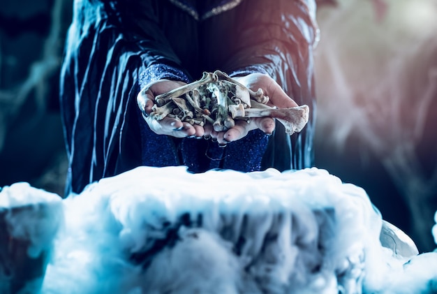 Close-up of a witch's hands holding bones above boiling water for a cooking poison soup.