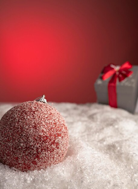 Close-up with christmas ball in snow, gift box and unfocused color background