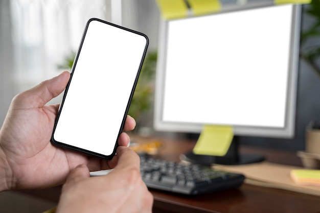 スマートフォンとノートパソコンのノートパソコンの空白の画面の前でスマートフォンを持っている人間の手でクローズアップ