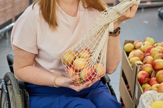 Primo piano di una donna che compra mele in un supermercato mentre è seduto su una sedia a rotelle