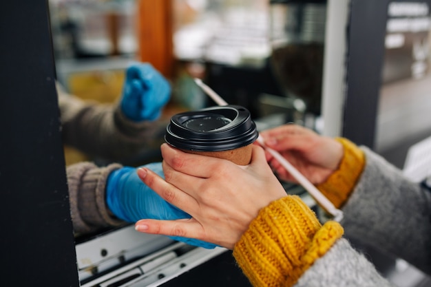 Close up of woman buying coffee and taking a paper cup from the barista seller's hands.