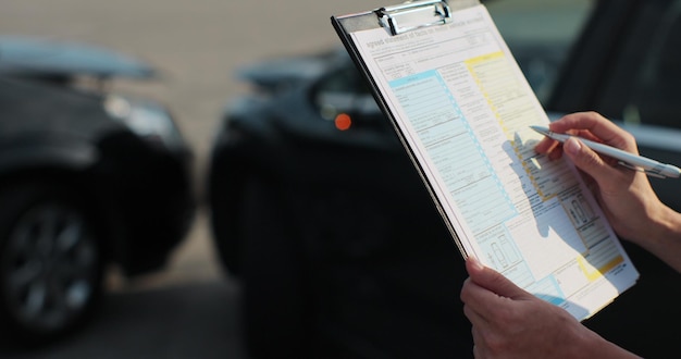 Close up of a woman car insurance agent inspecting damaged car with agreed statement of facts on motor vehical accident form Female filling in a car repair claim Insurance concept