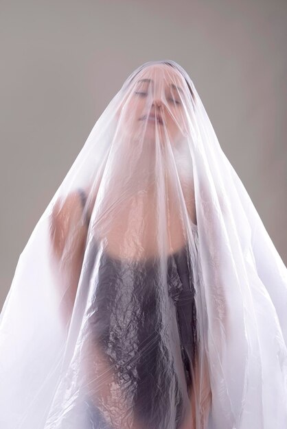 close-up of woman covered in plastic over gray background
