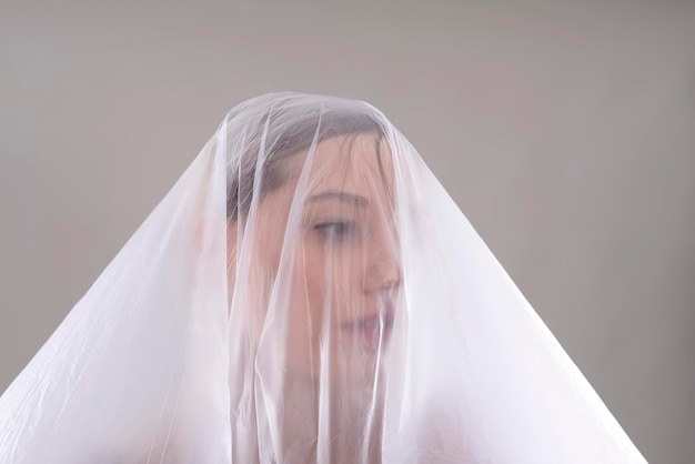 close-up of woman covered in plastic over gray background
