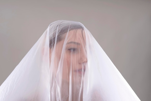 Photo close-up of woman covered in plastic over gray background