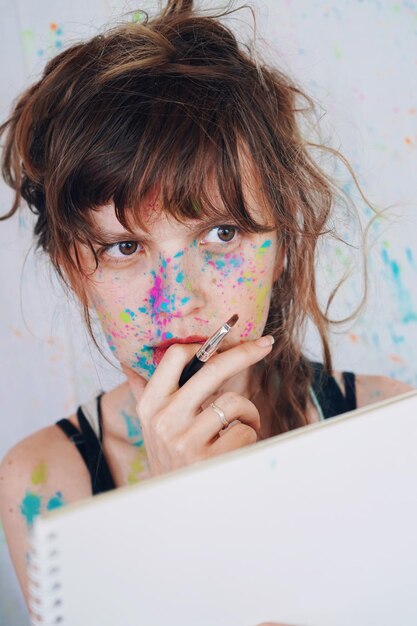 Photo close-up of woman covered in powder paint holding paintbrush and notebook