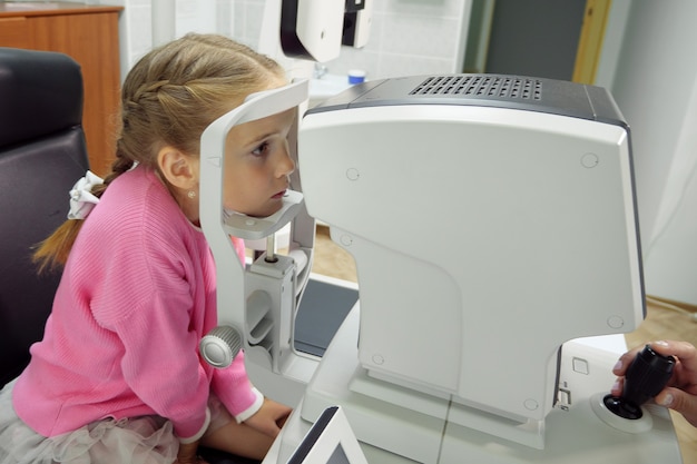 Close up of woman doctor working with the refractometer machine. A little girl having her eyes tested.