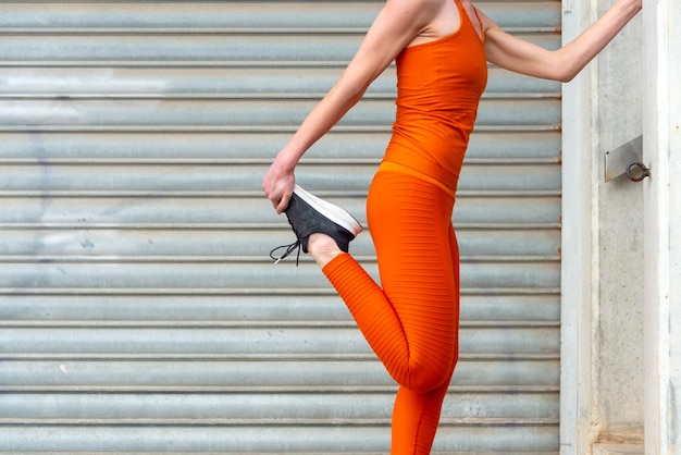 Близкий взгляд на женщину, занимающуюся растяжкой ног и разогревом в оранжевой спортивной одежде