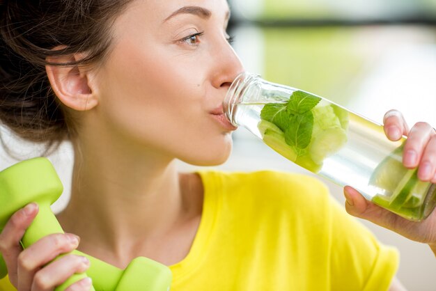 Close-up of a woman drinking water with mint, cucumber and lime during a workout with dumbbells. Detox dieting concept