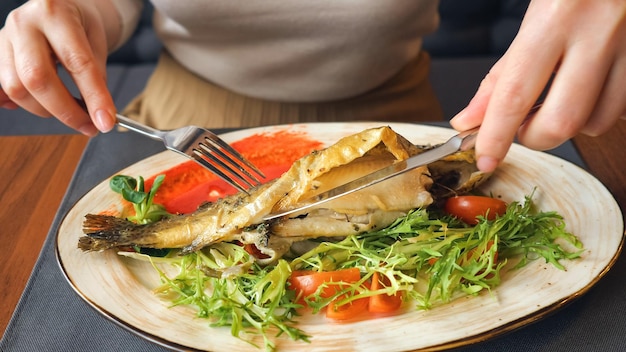 Photo close up of woman eating fish steak with knife and fork.