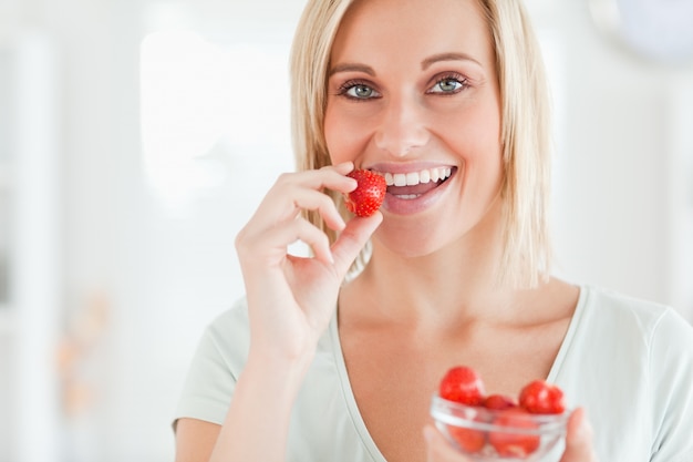 Close up of a woman eating strawberries looking into the camera in the kitchen