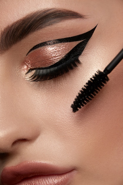 Close-up of woman eye with luxury golden make-up and mascara bru