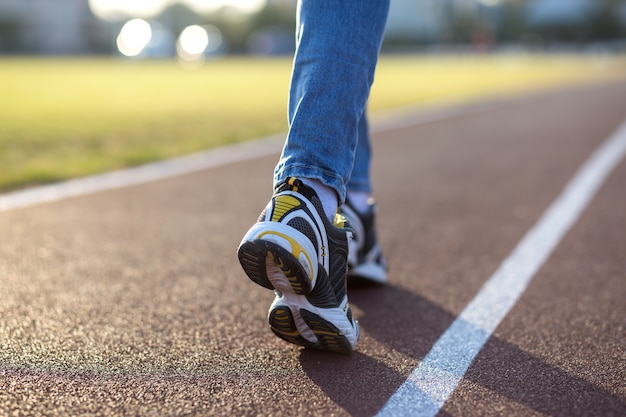 Close up of woman feet in sport sneakers and blue jeans on running lane on outdoor sports court.