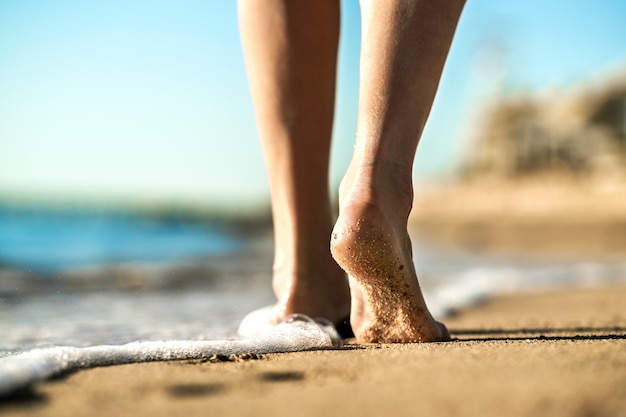 Chiuda in su dei piedi della donna che camminano a piedi nudi sulla sabbia lasciando impronte sulla spiaggia dorata. concetto di vacanza, viaggio e libertà. persone che si rilassano in estate.