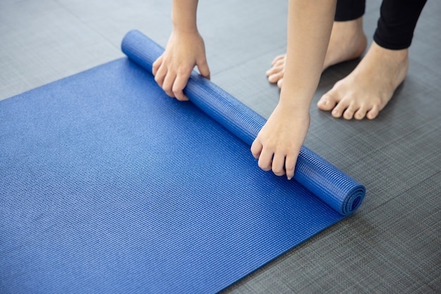 Foto primo piano sulla stuoia di yoga blu piegante della donna sul terreno dopo la lezione di yoha