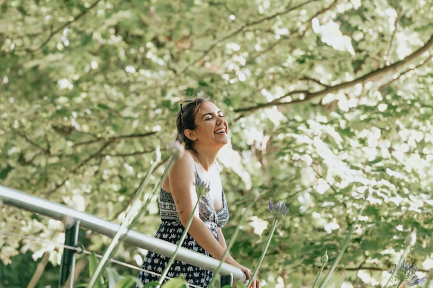 Close up of a woman in a forest near a handrail laughing and\
having fun with a dress looking away from camera, liberty freedom\
anxiety concept, self care, forest ambient