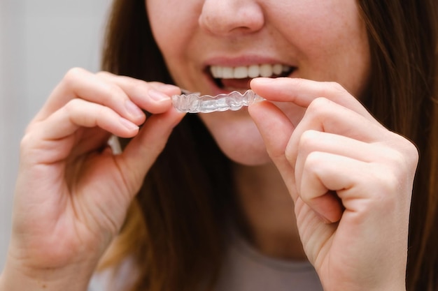 目に見えないプラスチック製の歯のアライナーを手に持ったバスルームの鏡の前で女性のクローズアップ中かっこをつけて美しく健康的な笑顔