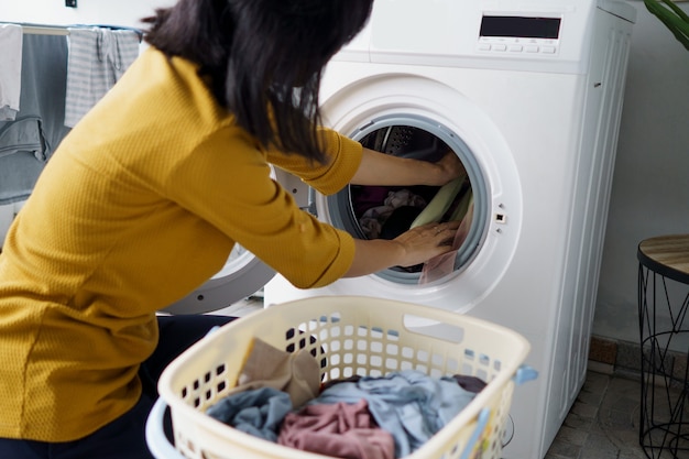 Close up of woman in front of the washing machine doing some laundry loading clothes inside