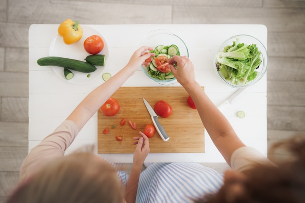 close up of a woman and girl cutting vegetables for salad in kitchen