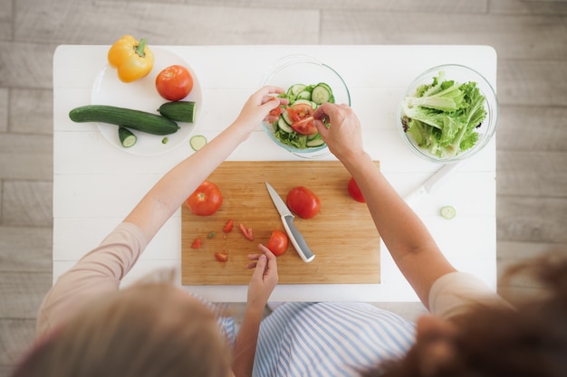 Close up of a woman and girl cutting vegetables for salad in kitchen