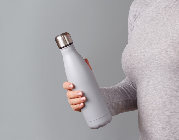 灰色のボトルを保持している灰色のTシャツの女性のクローズアップ