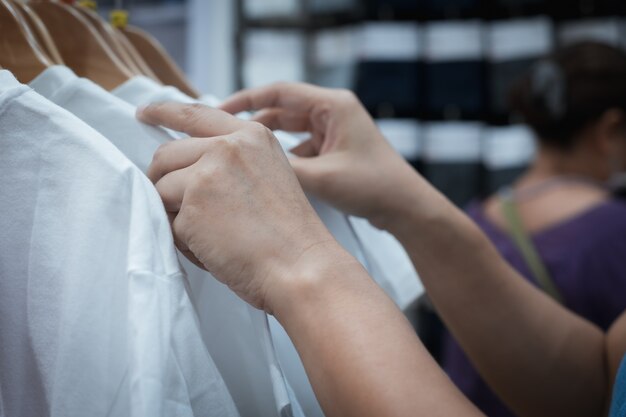 Chiuda in sulla mano della donna che sceglie i vestiti della maglietta di sconto nel centro commerciale