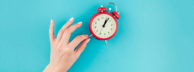 Photo close-up of woman hand holding alarm clock against blue background