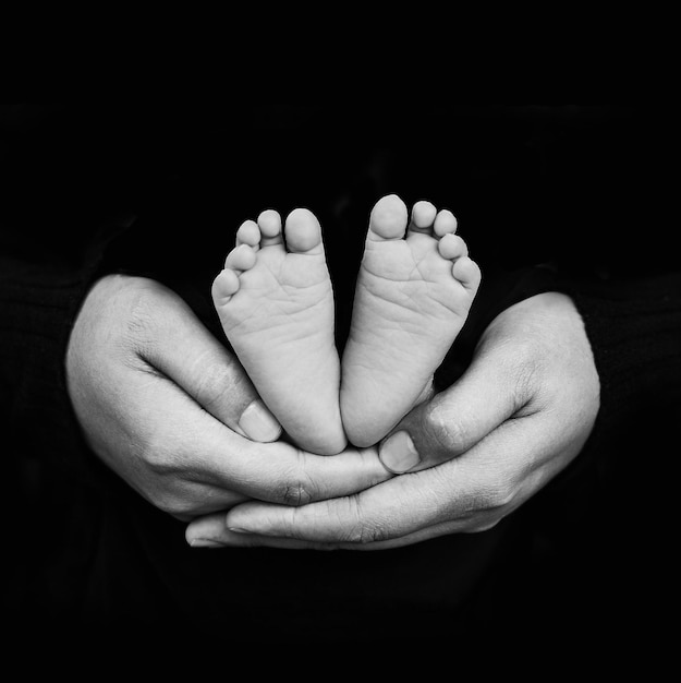 Foto close-up di una donna con la mano che tiene il bambino su uno sfondo nero