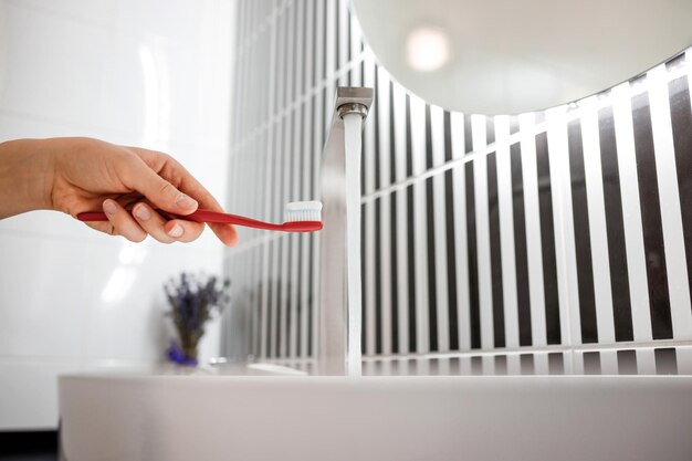 Close up of woman hand holding toothbrush with toothpaste while standing in bathroom