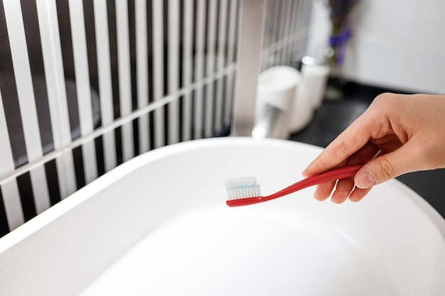 Close up of woman hand holding toothbrush with toothpaste while standing in bathroom