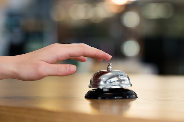 Close up of woman hand ringing bell at hotel at reception desk