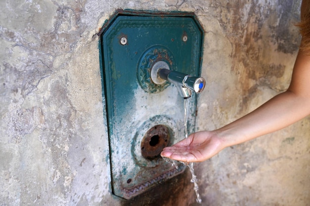 Close up of woman hand under running water from a fountain in the wall Thirsty and water crisis concept