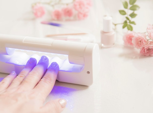 Close up of woman hand using led uv light lamp nail dryer to
harden uv nail polish