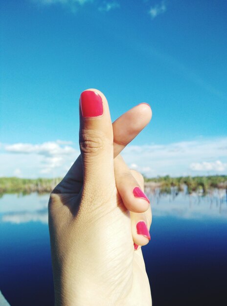 Close-up of woman hand over water against sky