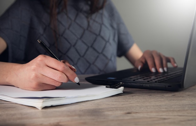 Close up of a woman hand writing a contract with a laptop