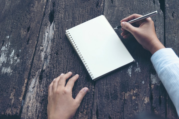 Close up woman hand writing on notebook. Woman writing on note paper diary on wooden table.