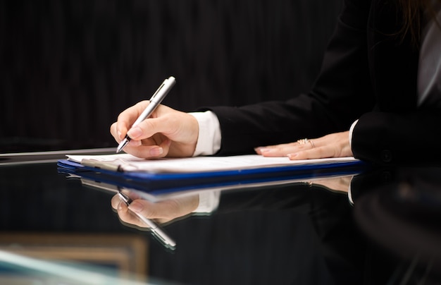 Close up of woman hands doing paperwork at glass desk. Secretary concept