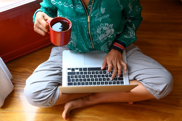 Primo piano mani di donna che tengono una tazza di tè e digitano sul laptop