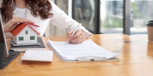close up of woman hands holding home model real estate brokerage contracts for sale and rent with insurance loan mortgage concepts