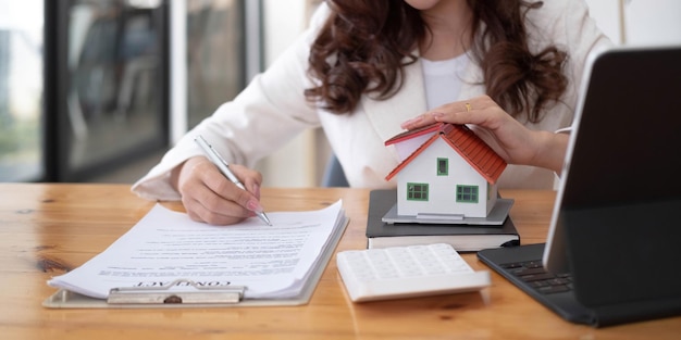 close up of woman hands holding home model real estate brokerage contracts for sale and rent with insurance loan mortgage concepts