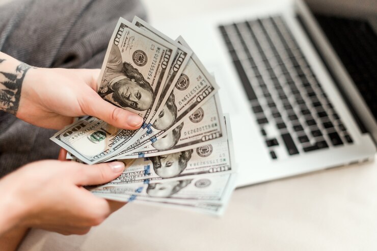 Photo close up of woman hands holding new dollar bills she earned working from laptop at home online
