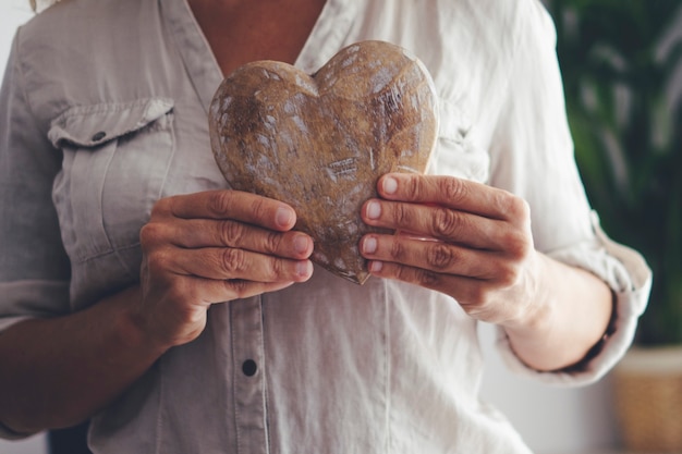 Close up of woman hands holding wooden heart. Concept of heart attack prevention and healthy people care. Mature female people indoors