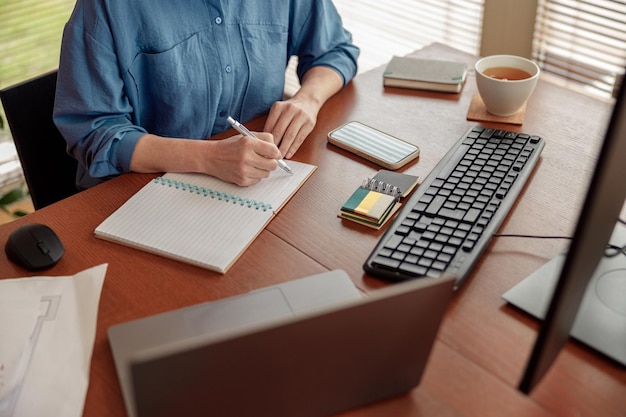 Close up of woman hands taking notes while working in cozy home office remotely