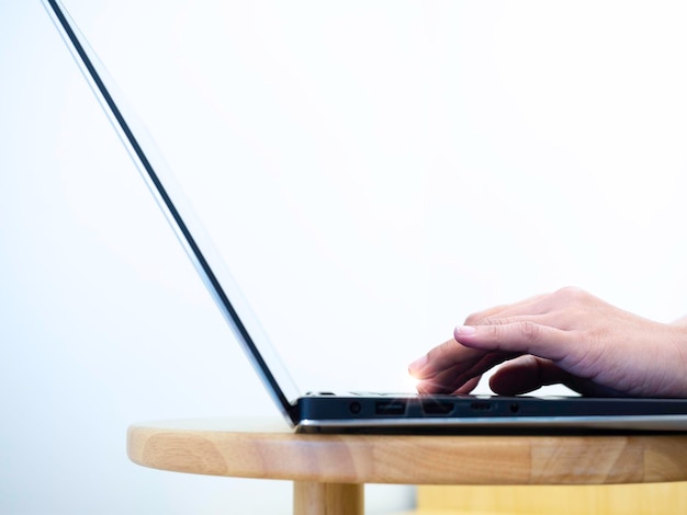 Primo piano delle mani della donna che digitano sulla tastiera del computer portatile sul tavolo rotondo di legno su sfondo bianco con spazio per la copia. concetto di business online, lavorare con la tecnologia, lavorare da casa, scrivere e-mail.