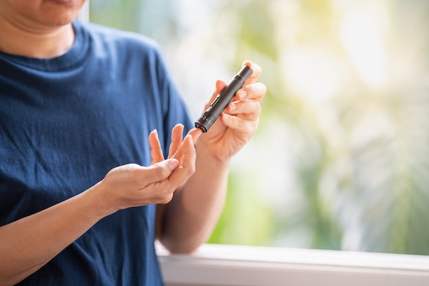 Close up of woman hands using lancet on finger to check blood sugar level by Glucose meter. Use as Medicine, diabetes, glycemia, health care and people concept.