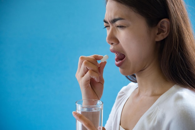 Close-up of woman having medicine against blue background