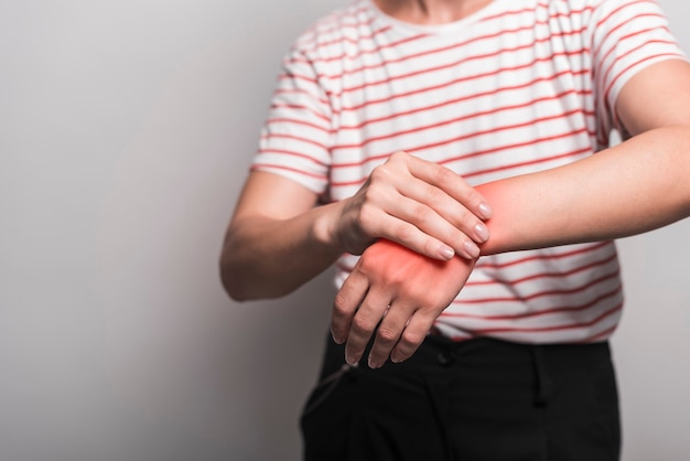 Foto primo piano della donna che ha dolore in polso contro fondo grigio