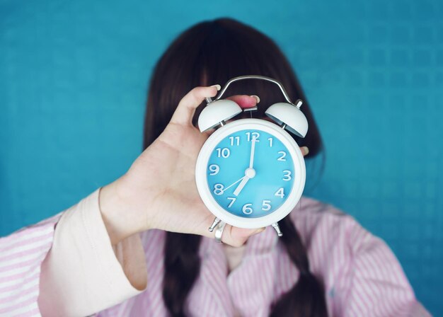顔の前で目覚まし時計を握っている女性のクローズアップ