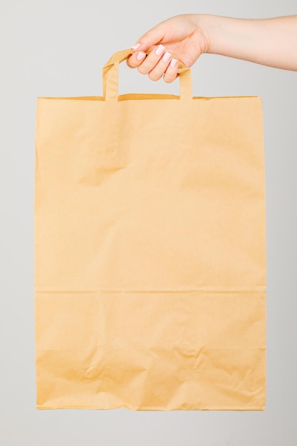 Close up of a woman holding a brown empty paper bag isolated on a grey background Service delivery concept