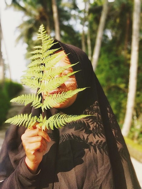 Photo close-up of woman holding fern over face